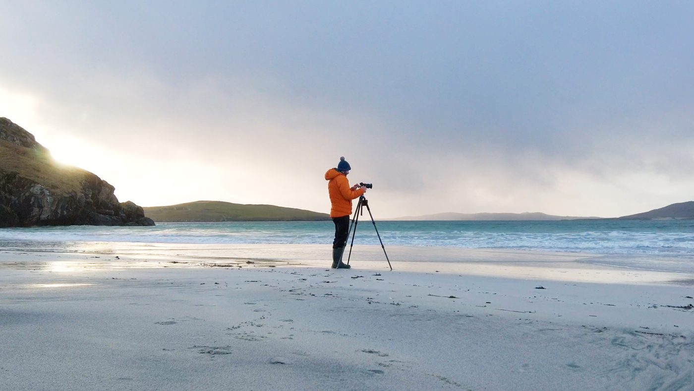 Photographer in an orange jacket on a Hebridean beach